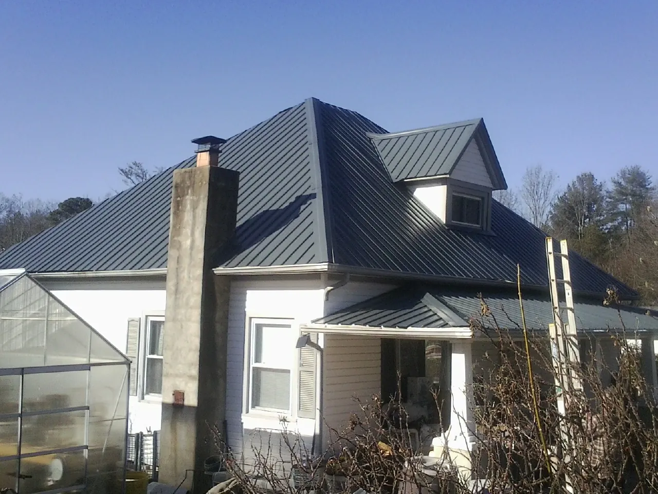 Dark blue standing seam metal roof on a white farmhouse with dormer — Slate & Tile Roof Repair by Roofing Brothers in Castella