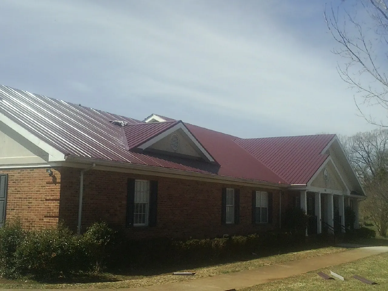 Red metal roof with gabled entries on a long brick building, from a Hail Damage Roof Repair job in Castella