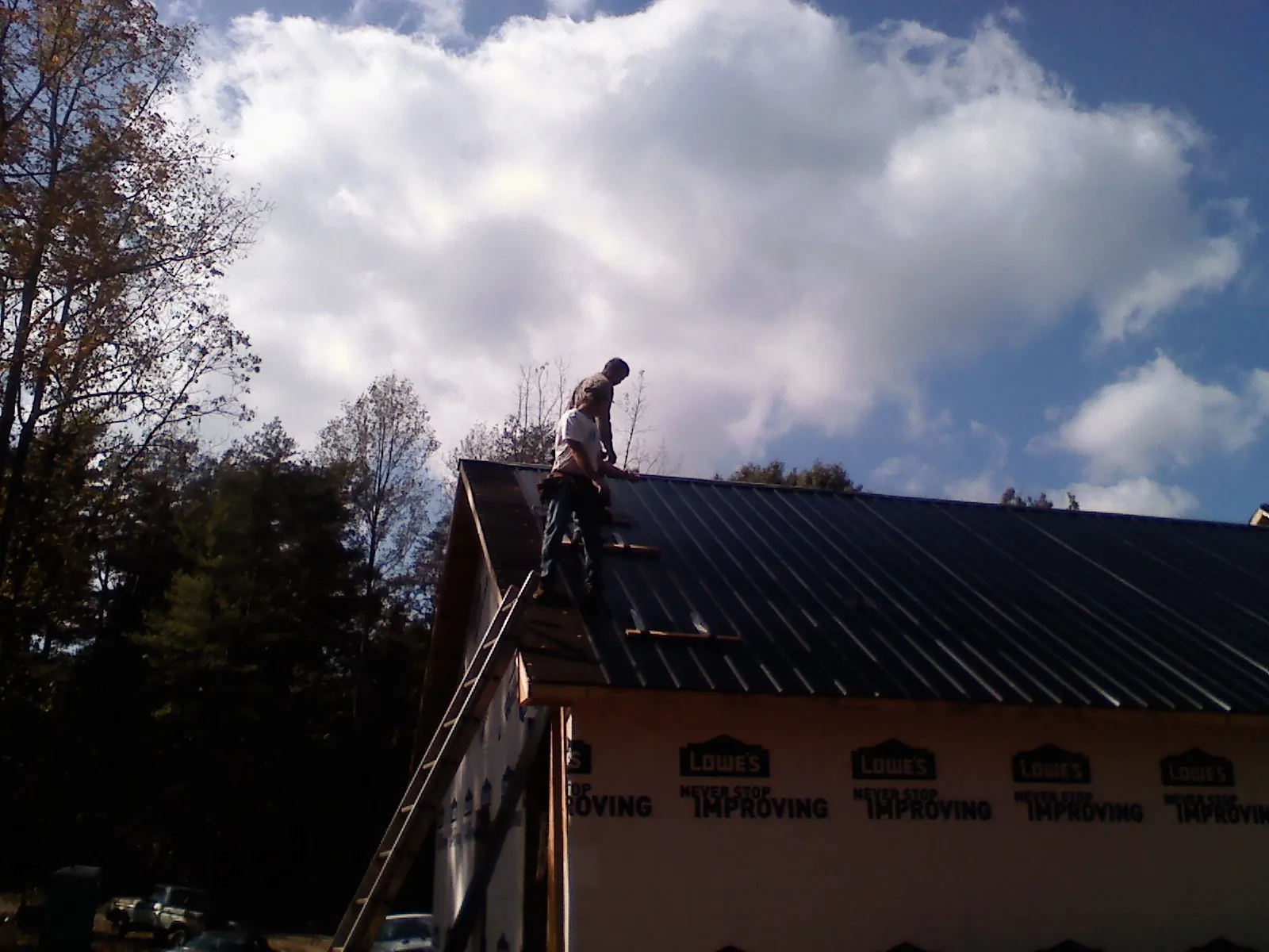 Roofer fastening dark metal panels high against a cloudy sky, from a Roof Inspection job in Castella