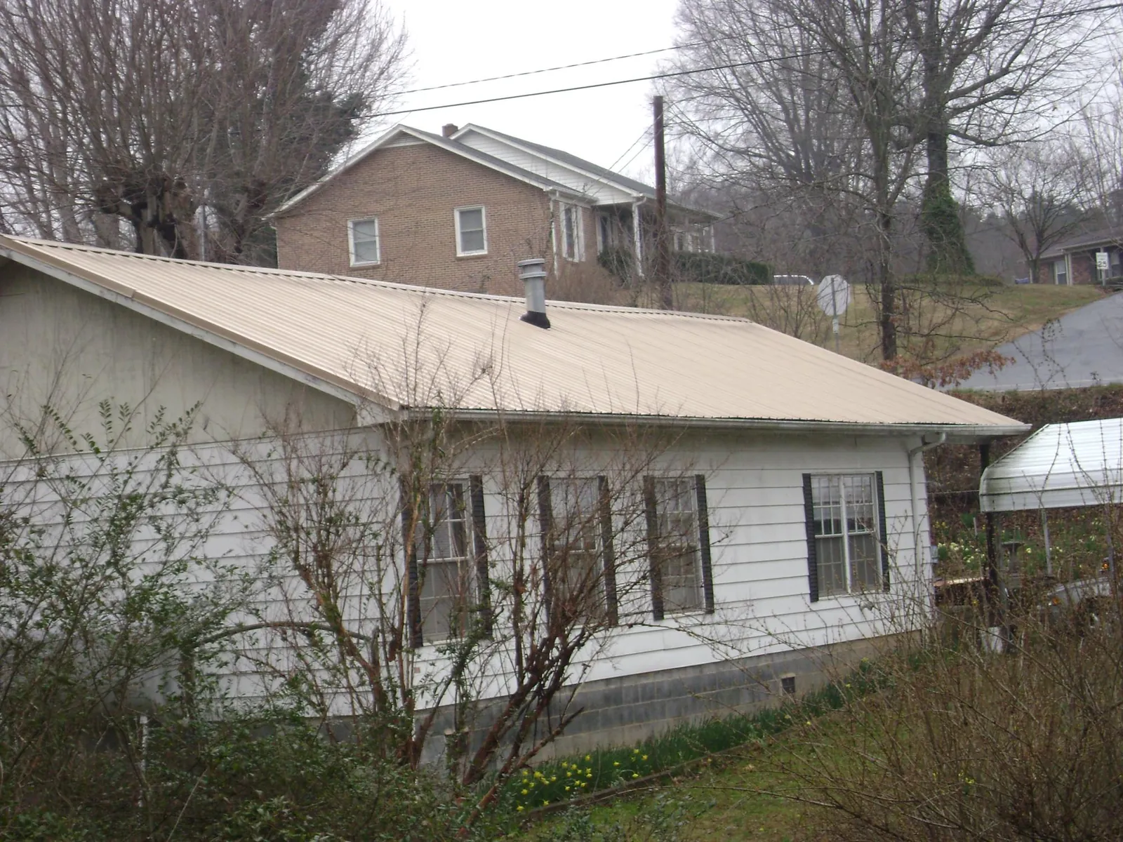 Tan metal roof on a white sided house set into a hillside — Commercial Roofing by Roofing Brothers in Castella